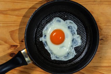Cooking roasted eggs for breakfast, another egg is driven into pan for fried eggs.