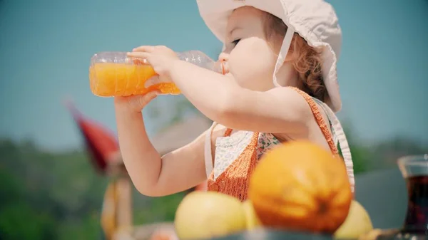 Little girl wearing orange clothes drinks orange juice