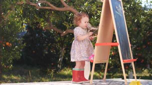 Kleines Mädchen Roten Regenstiefeln Malt Auf Staffelei — Stockvideo