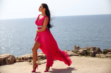 Sahilde uzun kırmızı elbiseli güzel siyah saçlı kız yaz gününün tadını çıkarıyor.