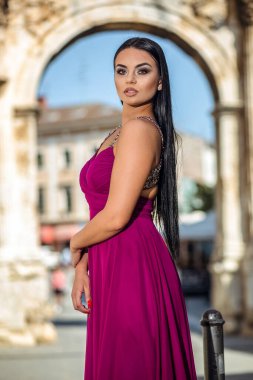 Uzun kırmızı elbiseli güzel siyah kadın şehrin eski bölümünde yürüyor.