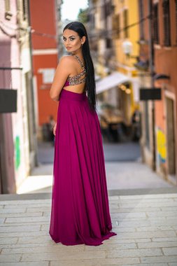 Uzun kırmızı elbiseli güzel siyah kadın şehrin eski bölümünde yürüyor.