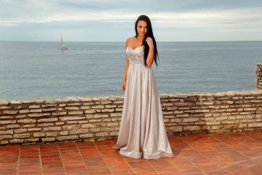 Uzun beyaz elbiseli güzel siyah saçlı kadın denize bakmaktan hoşlanıyor.