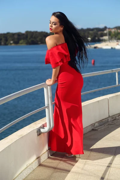 長い赤いドレスを着た美しい若い黒髪の女性は 海を見てヨットで楽しんでいます — ストック写真