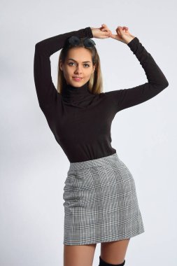 Young woman in studio in brown roll top and mini skirt, posing on white background