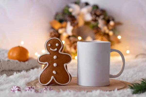 クリスマスの居心地の良い組成 ジンジャーブレッドマンクッキー 紅茶やコーヒーの白いカップ 白い毛布の上にライト付きクリスマスリース 選択的焦点 ストック画像