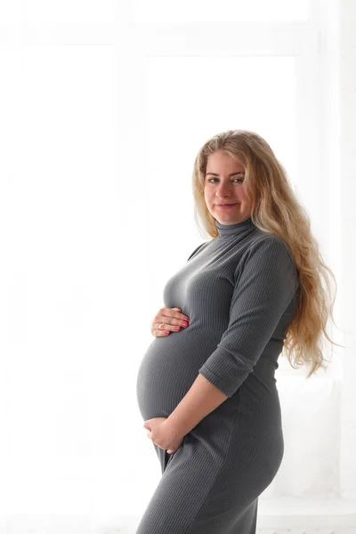 美丽的孕妇抱着肚子站在窗边 看着摄像机 选择焦点 复制空间 怀孕和生育的概念 — 图库照片