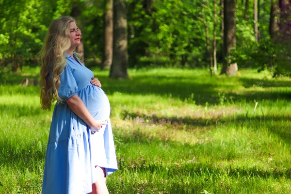 緑の森の芝生に彼女の腹を保持長いブロンドの髪を持つ若い美しい妊婦 テキストのスペースをコピーします 選択フォーカス 出産の概念 — ストック写真