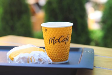 Vinnitsya, Ukrayna... 08 Temmuz 2024: Sarı McCafe bardağı, dokulu bir yüzey ve McCafe logosu, bir tepsinin üzerine yerleştirilmiş bir hamburger..