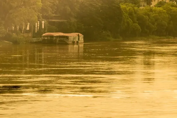 Pontoon boat docked on riverbank in golden evening sun.