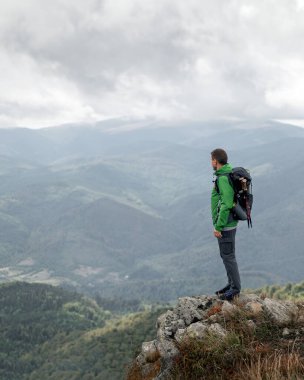Yeşil ceketli bir dağın tepesinde duran bir gezgin.