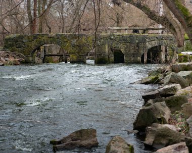 Stone bridge - a fragment of a mill. The flow of a rapid river rushed into a mill wheel.Water wheel and old mill in the woods. clipart