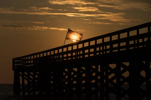 サンセットは フロリダ州タンパのノース レディントン ショアーズ近くの漁港で アメリカの旗に輝くスポットライトを当てました ストック画像