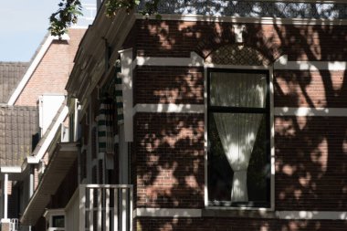Utrecht 'teki eski tuğla köşkün pencerelerinde beyaz perdeler, güneş ışığı ve gölgeler duvarı kaplıyor, Utrecht, Amsterdam
