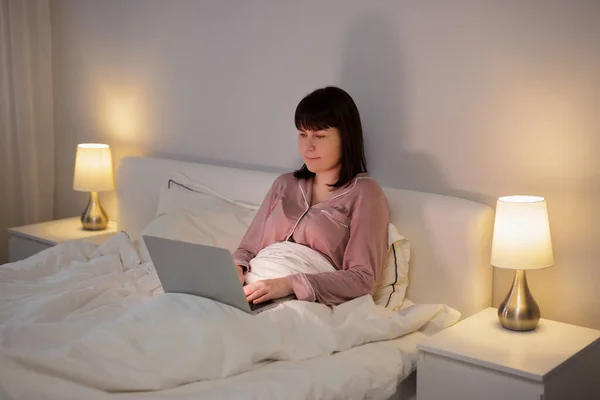 年轻女人躺在床上用笔记本电脑 — 图库照片