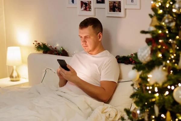 Portrét Mladého Muže Pomocí Smartphonu Zdobené Ložnici Vánoční Stromeček — Stock fotografie
