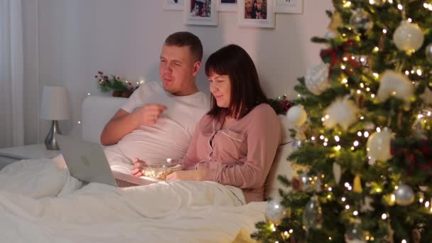 家庭和圣诞节的概念 快乐的夫妻一起看电影 在装饰过的圣诞树旁吃爆米花 — 图库视频影像