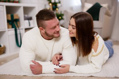 Halıya uzanmış, Noel süslemeli odada birbirine bakan bir çift.