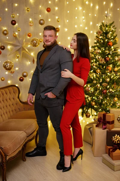 プレゼント付きクリスマスツリーの近くにポーズをとるお祝い服のスタイリッシュなカップル — ストック写真