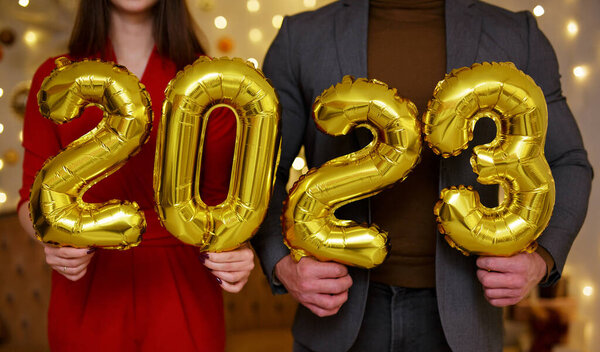 Close up of male and female hands holding golden 2023 balloons