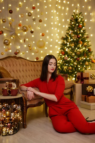 美しいです若いです女性で赤いスーツで座っているクリスマスツリーの近くにプレゼント — ストック写真