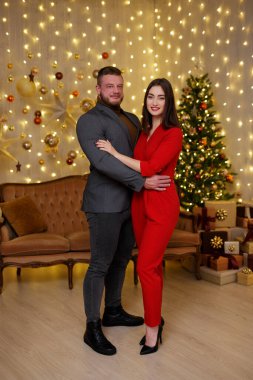 Noel süslemeli odada, şenlikli kıyafetler içinde güzel genç bir çift.