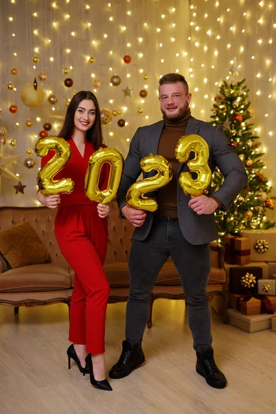 陽気なカップル見ますカメラとともに黄金2023風船でクリスマス装飾された部屋 — ストック写真