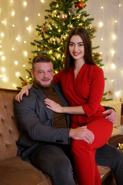穿着红衣的女人坐在圣诞树旁的男性腿上 — 图库照片