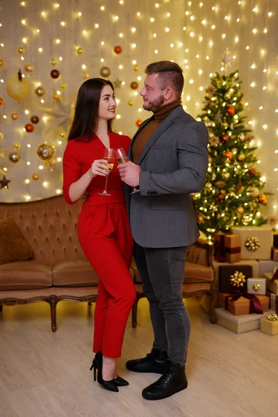 若いです男と女でお祝いの服でシャンパンと手でクリスマスツリーの近く — ストック写真