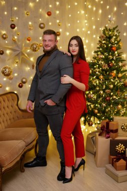 Noel ağacının yanında hediyelerle poz veren neşeli elbiseli bir çift.