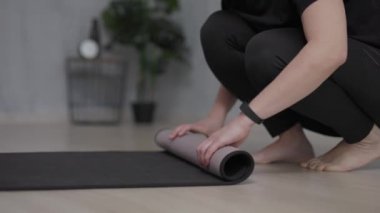 close up of woman rolls out a yoga mat on the floor at home or training room