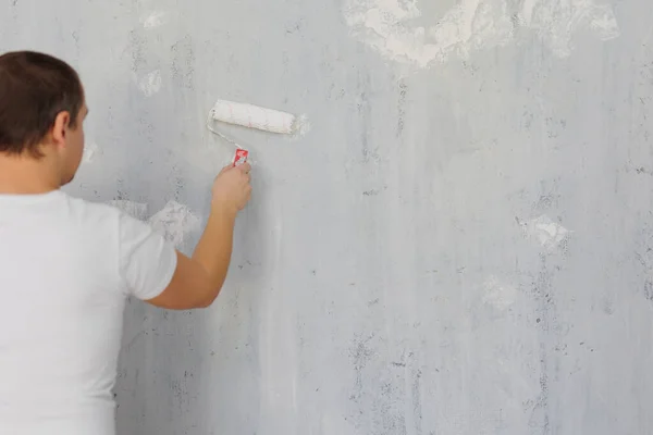 back view of painter man painting the wall with paint roller, copy space over grey  wall