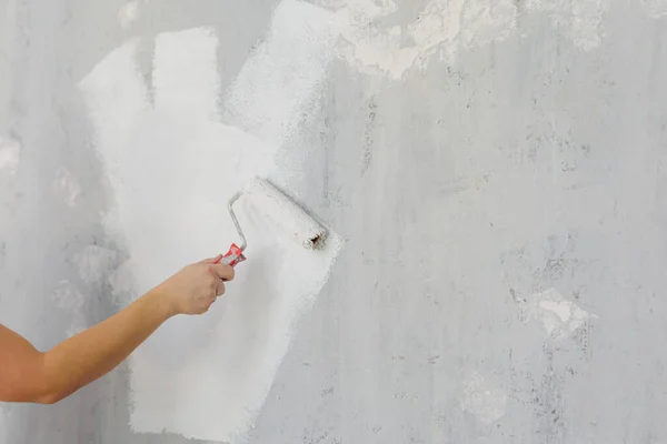 close up of male hand painting wall into white color with a roller, copy space over grey wall background