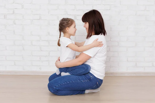 Happy mother and daughter sitting on the floor in jeans and white t-shirts