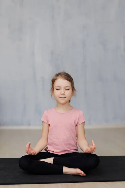 可爱的小女孩在家里的瑜伽垫上做瑜伽练习 复制灰色墙壁背景上的空间 — 图库照片