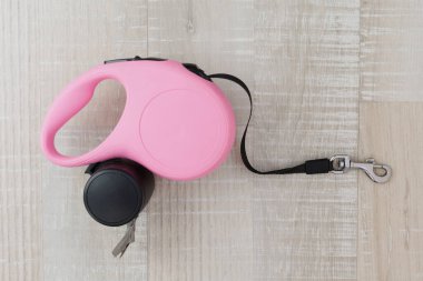 Ahşap arka planda çöp torbaları olan pembe geri çekilebilir köpek tasması.