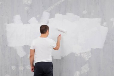Boyacı gri duvarı beyaz boya rulosuyla beyaza boyuyor, duvardaki boşluğu kopyalıyor.