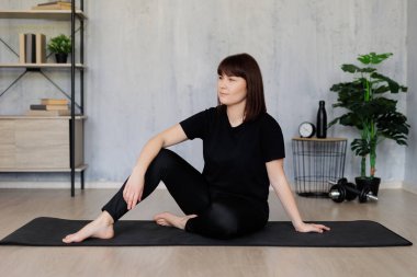Yoga ve meditasyon konsepti - eğitim öncesi veya sonrası yoga minderinde oturan genç kadın