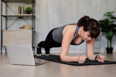 Bilgisayarda online eğitim gören ve evde spor yapan genç bir kadın.