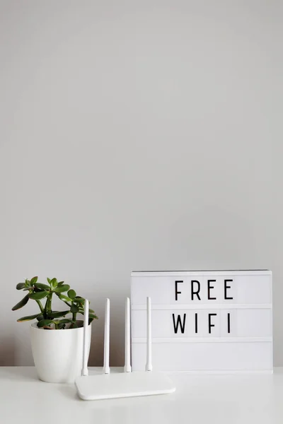 stock image White router, plant and lightbox with free wifi text on table with copy space