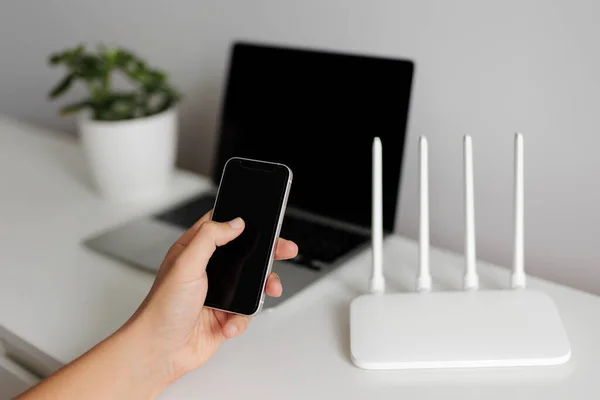 Stock image Internet connection concept - hand with phone in the foreground and computer with white router on background