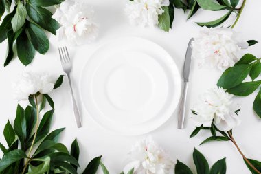 Beyaz tabak, çatal bıçak ve şakayık masalı bir ziyafet masası.