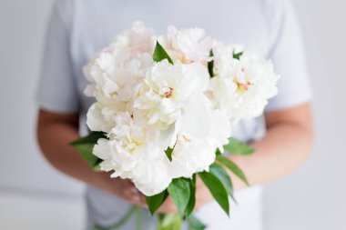 Mavi tişörtlü bir adam elinde beyaz şakayık buketi tutuyor.