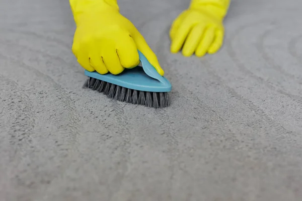 cleaning concept - hands in yellow rubber gloves cleaning grey carpet with brush, copy space over carpet