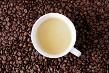 Kahve çekirdeklerinin koyu arka planında bir fincandaki kahvenin üst görüntüsü.