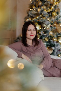 Kırmızı dudaklı güzel bir kadın Noel süsleme odasında koltukta oturuyor.