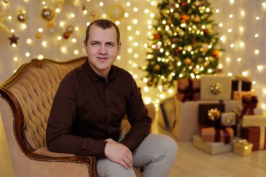 Dekorasyon odasındaki noel ağacının yanındaki koltukta oturan adam.
