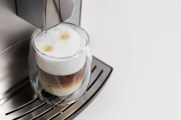 close up of double  glass cup of latte on coffee machine and copy space over white table