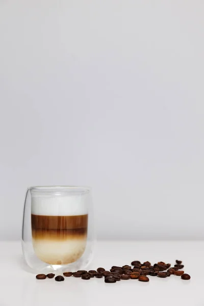 close up of double glass cup of fresh latte coffee with coffee beans on white table and copy space