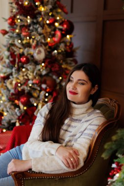 Işıklı bir Noel ağacının yanında süveter giyen bir kadın.